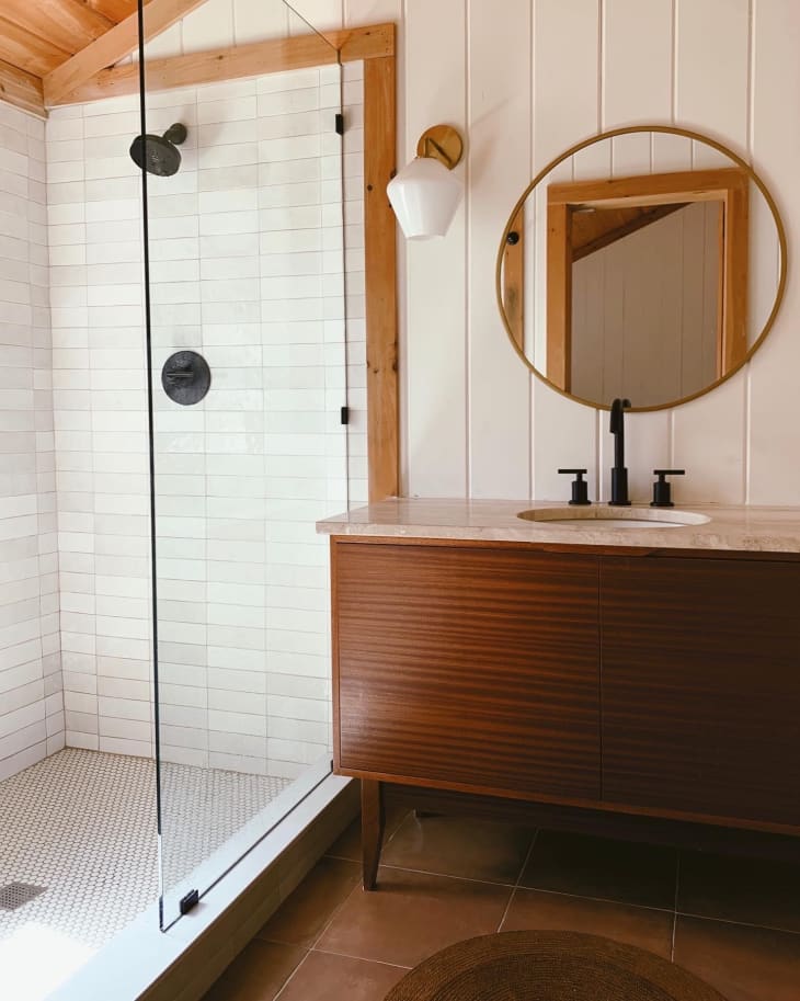 Modern cabin farmhouse style bathroom with white panel walls, terracotta tile, teak wood vanity, and white tile shower.