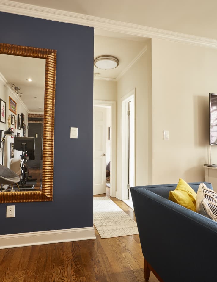 Giant mirror with thick gold frame hanging on a deep blue accent wall