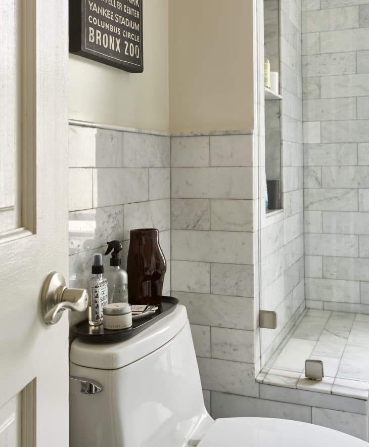 Modern bathroom with marble subway tiles and a tray of accessories on top of a toilet tank