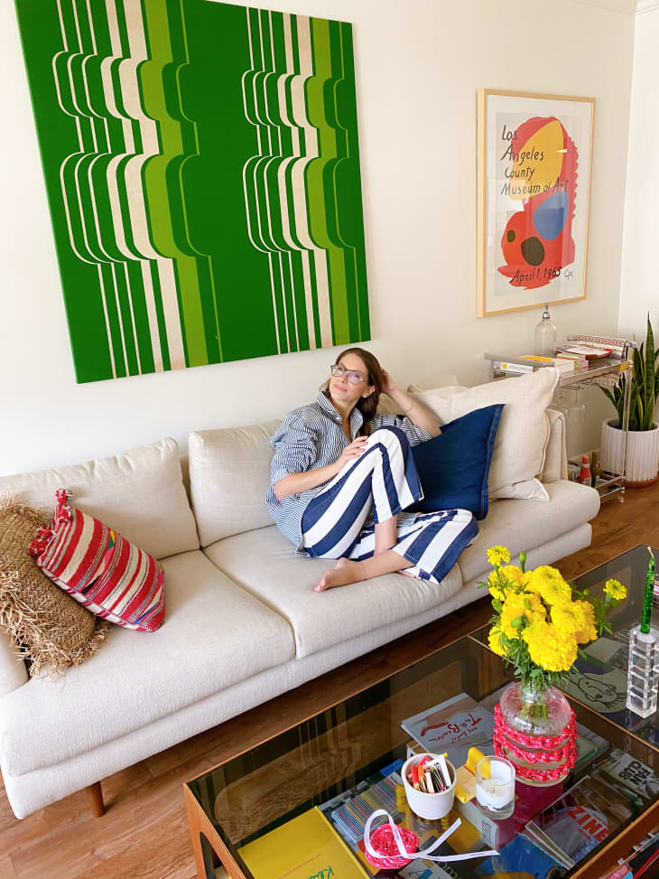 Woman in blue and white striped pants sitting on a modern white sofa with vintage green 1970s art hanging on the wall above