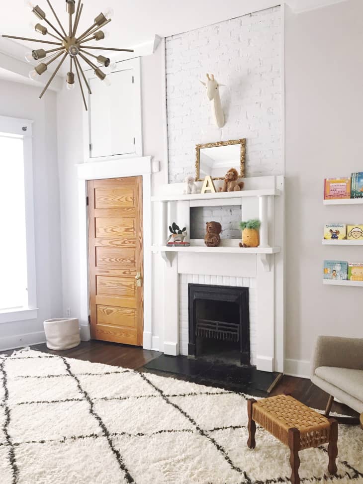 All white nursery with sputnik chandelier, beni ourain rug, fireplace, and eclectic furniture