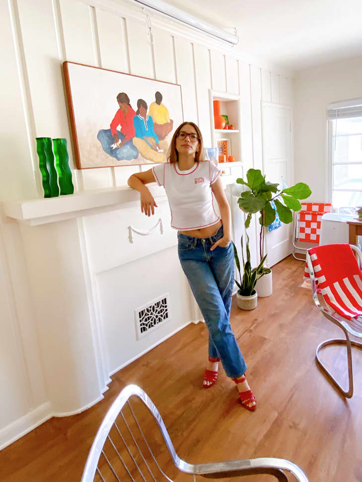 Woman in jeans and t-shirt leaning against a white modern fireplace mantel with art hanging on the wall above