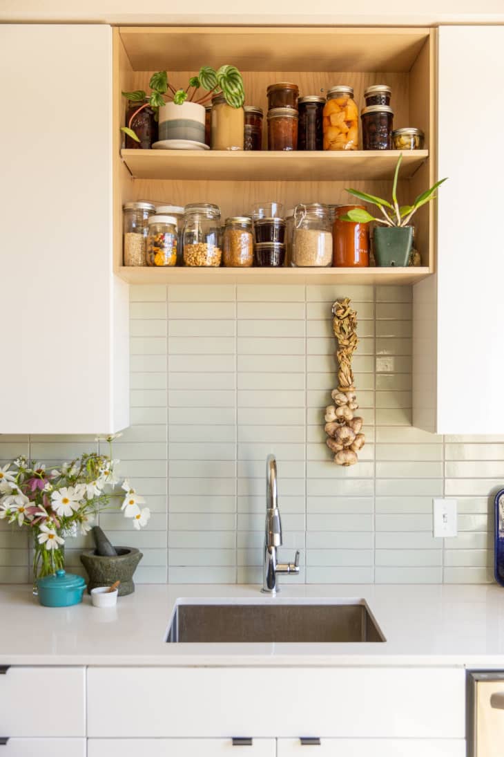 Modern wooden open shelving above a kitchen sink and backsplash filled with jars of dried goods