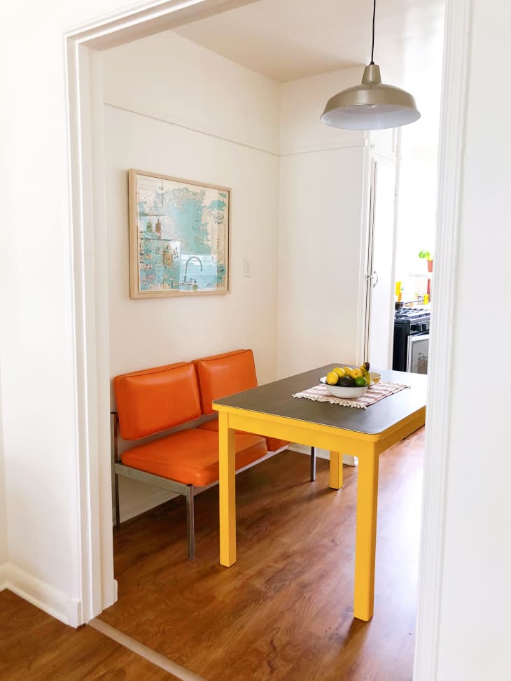 Minimal modern dining nook with white walls, orange vinyl loveseat and yellow table