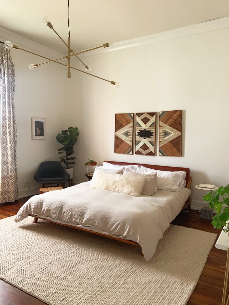 Neutral bohemian bedroom with modern brass chandelier and wood art piece above bed