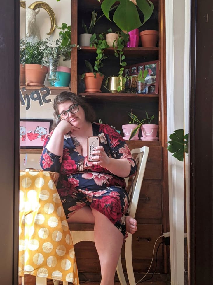 Woman taking mirror selfie in front of bookshelf with plants on it