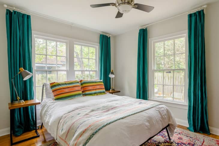 Bedroom with several windows, white bedding, and teal curtains