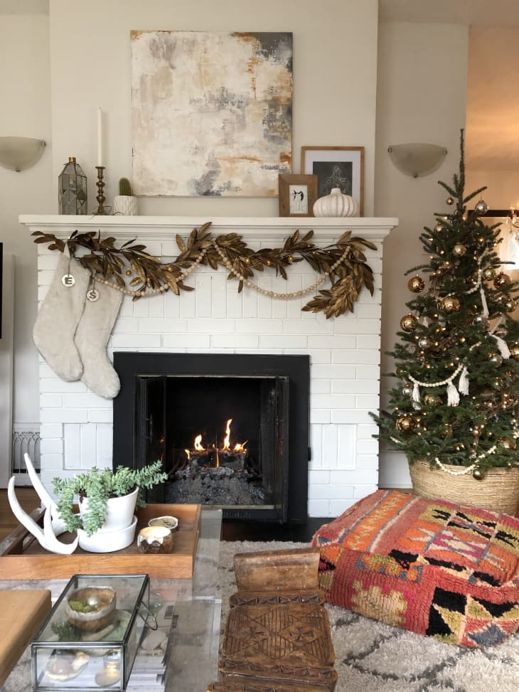 Boho living room with Christmas tree next to garland- and stocking-adorned fireplace