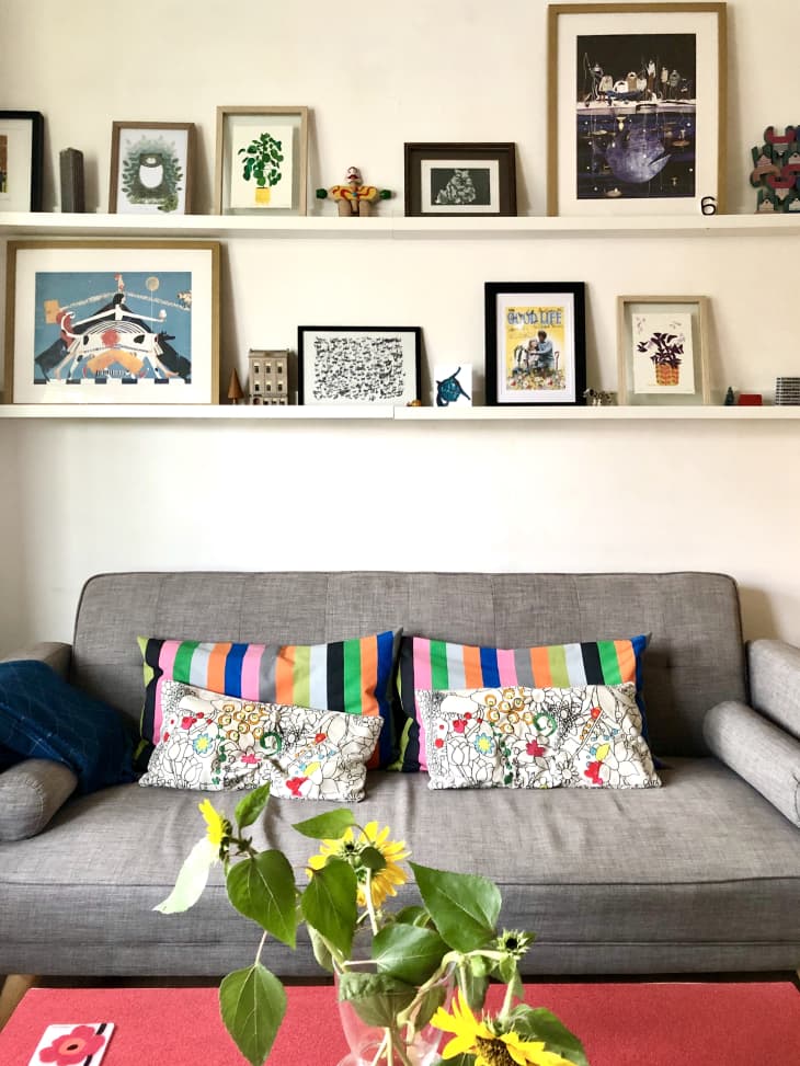 Gray sofa with rainbow stripe pillows and pictures on shelves above