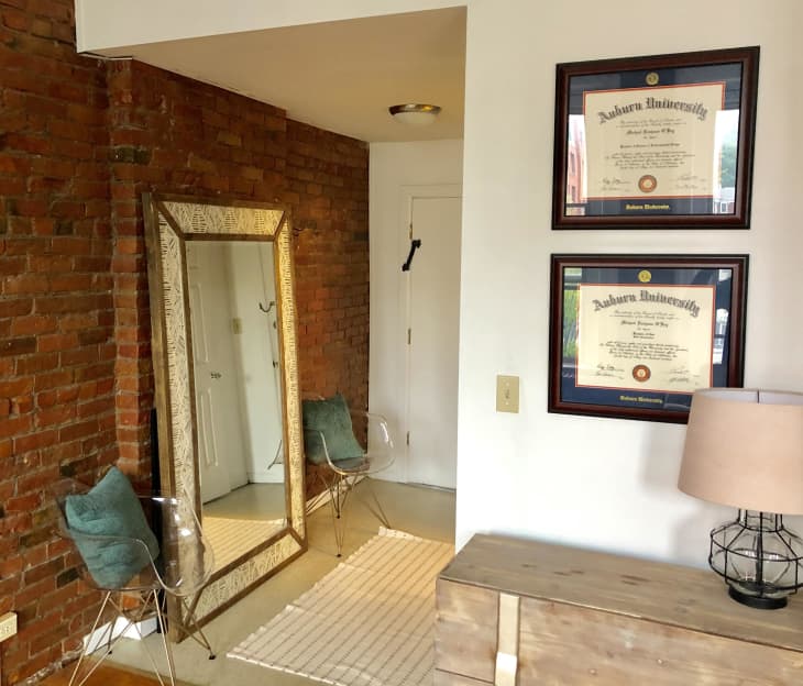 Entryway with floor-length mirror, clear lucite chairs, and diplomas hanging on wall