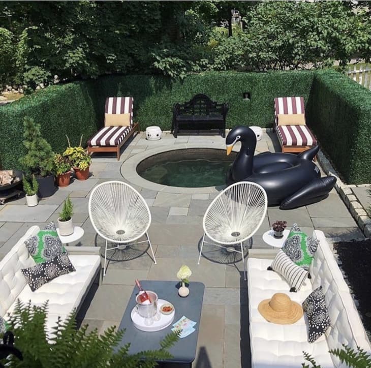 Patio space decked with white sofas and chairs, striped loungers, and a black swan pool float