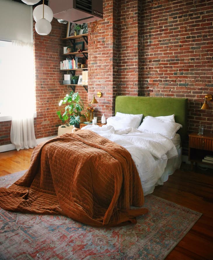房间砖墙，床上有绿色天鹅绒床头板