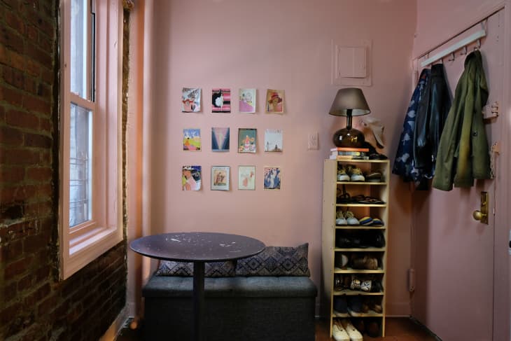 Small kitchen with bench, round table, shoe and coat storage, and artwork in grid hanging on pink wall