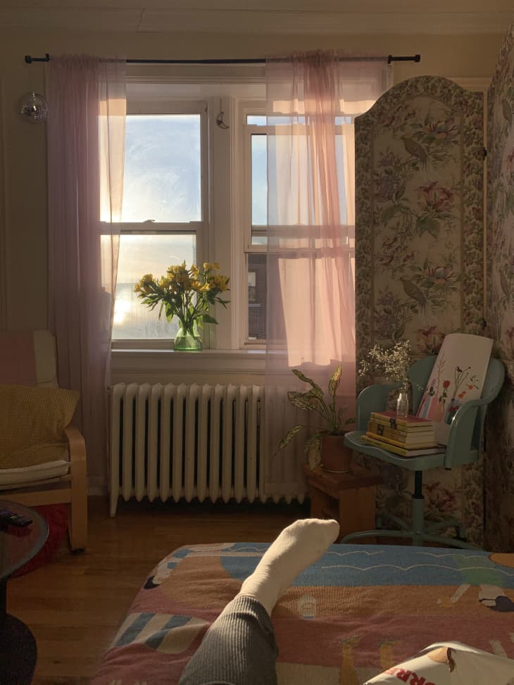 Bedroom with floral room divider and radiator under window with sheer curtains