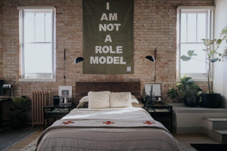 Bedroom with brick wall and green tapestry that says "I AM NOT A ROLE MODEL"