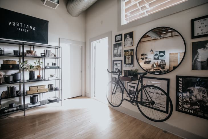 Corner of space with gallery wall with black and white art, circular mirror, and bicycle shelf on right and organized, accessorized shelf on left