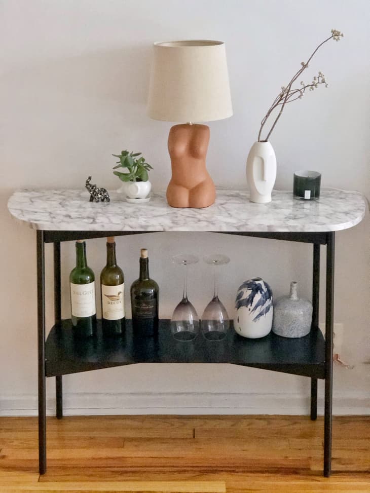Console table with wine and wine glasses on lower shelf, lamp and plants on top