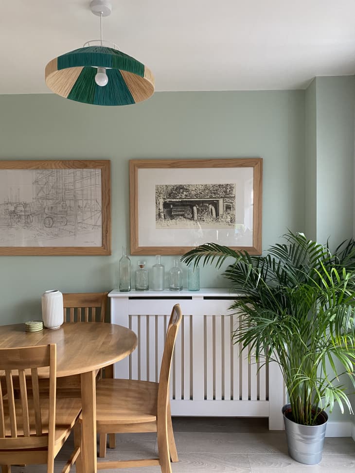 Dining area with light green walls, wooden table, white sideboard, and green pendant light