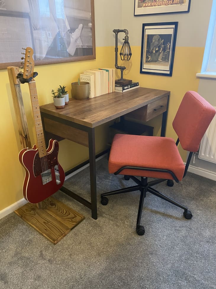 Wooden desk and guitar in corner of carpeted room