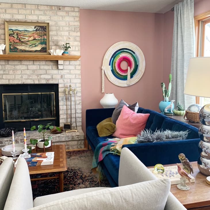 Living room with brick fireplace, pink walls, blue sofa, and fiber art on wall