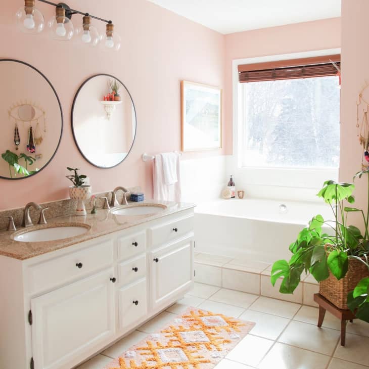 Bathroom with pink walls, two sinks, two circular mirrors, and a bathtub