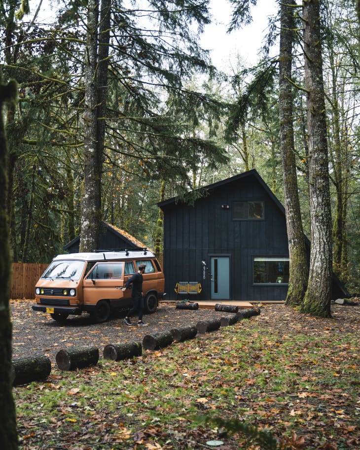 Cool old orange van parked by black cabin with blue door