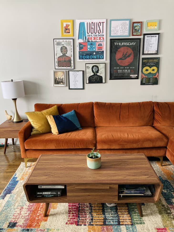 Living room with orange velvet sofa, mid-century tables, and concert artwork on wall