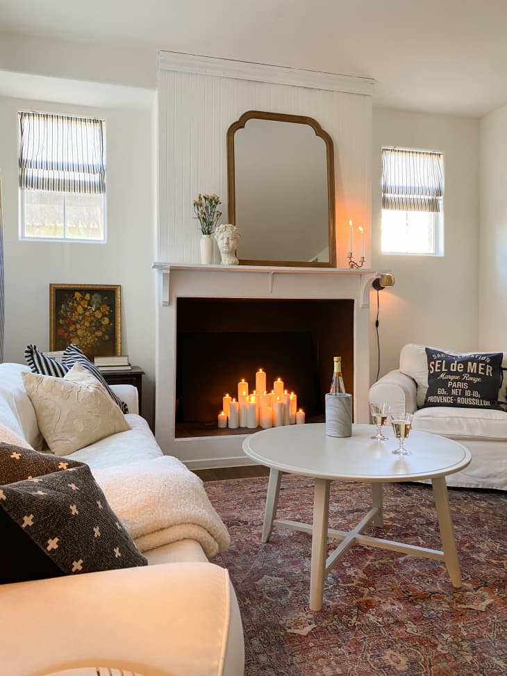 Living room with vintage-looking rug and mirror above fireplace with candles inside