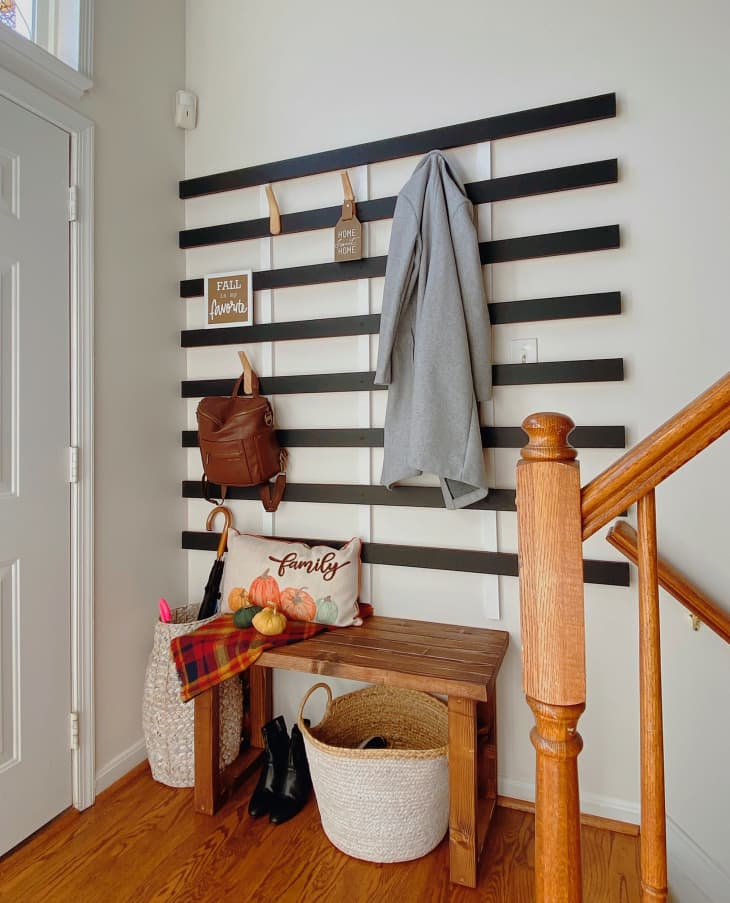 Entryway with coat and bags hanging on hooks connected to black wooden slats
