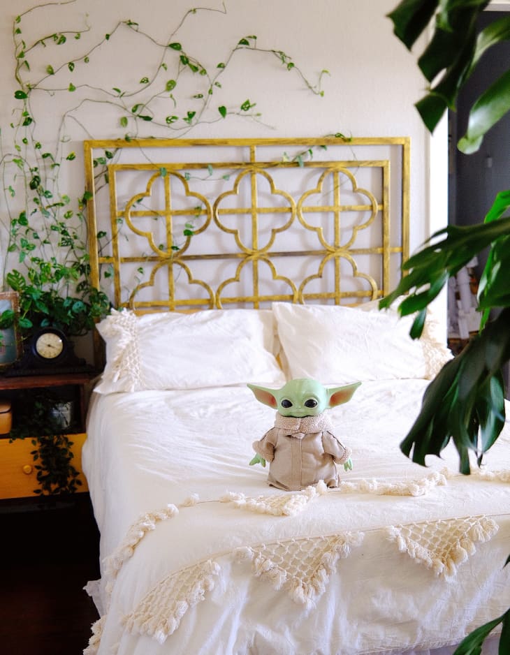 Baby Yoda toy on bed with white linens and gold metal headboard