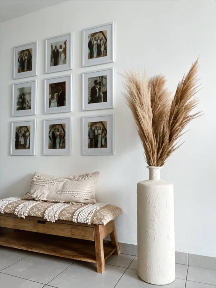 Off-white textured vase holding dried stems next to bench and photo wall