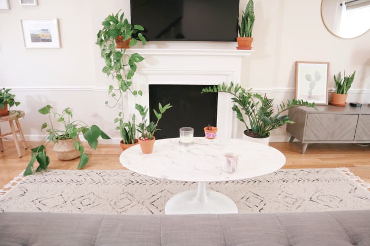 Round marble coffee table in front of fireplace in plant-filled living room