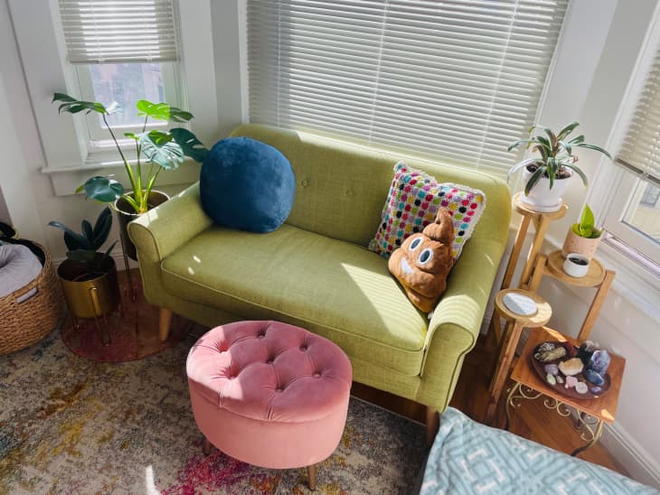 Green loveseat with emoji pillow and pink footstool in front of bay window