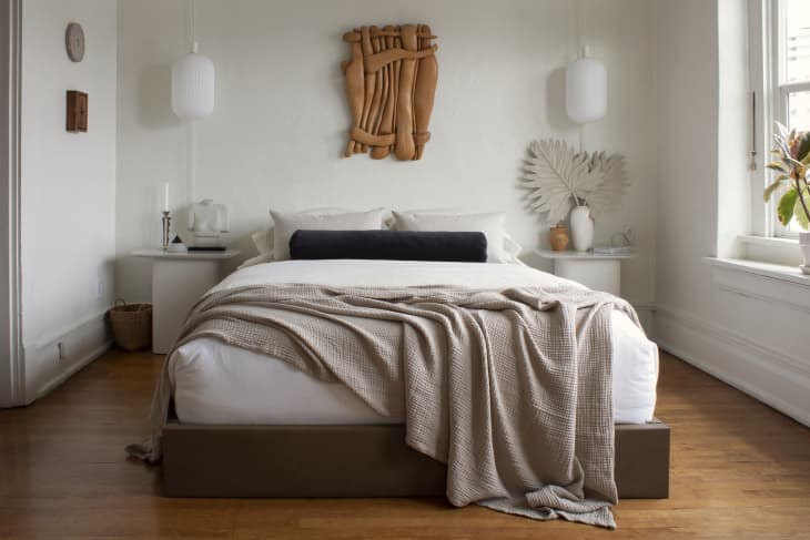 Bright white bedroom with wooden artwork on the wall above head