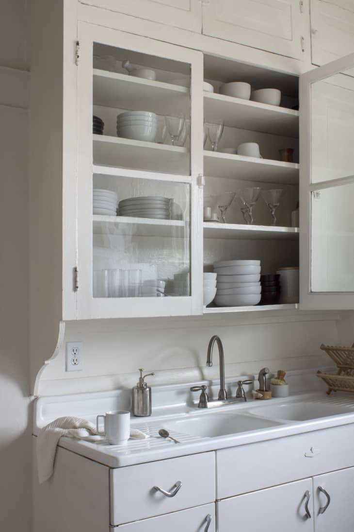 White kitchen cabinet holding white dishes with sink below