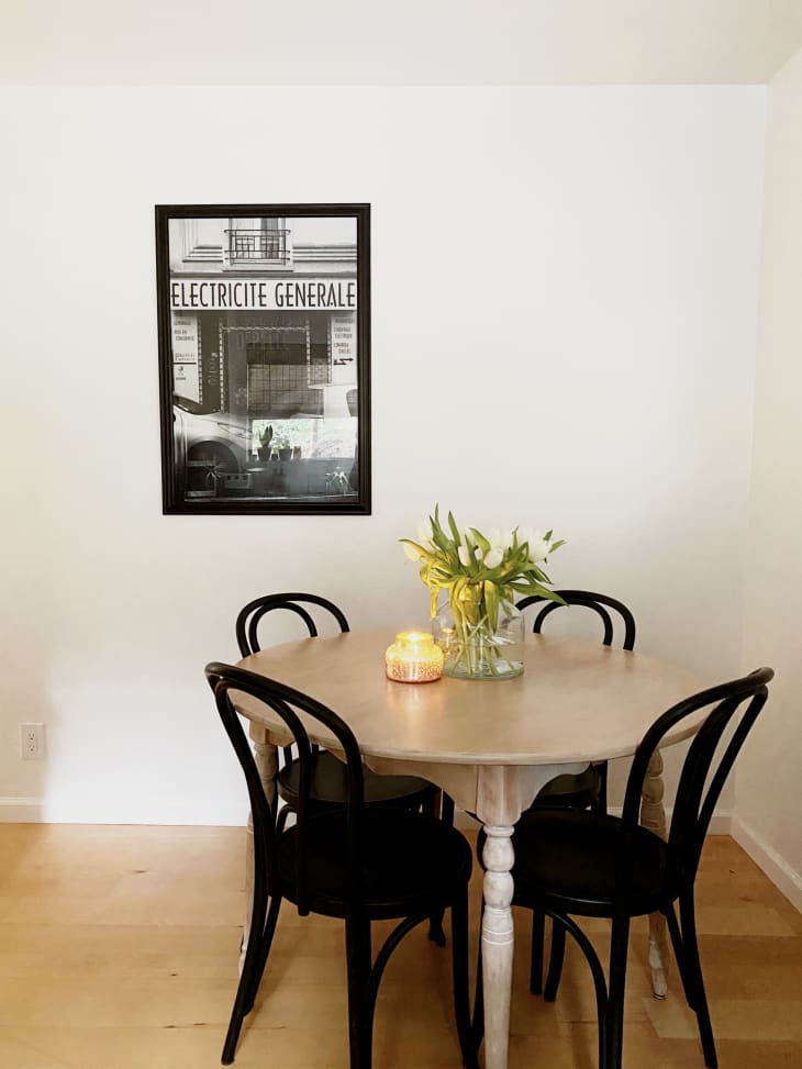Round dining table with black Thonet-style chairs next to framed black-and-white photograph on wall
