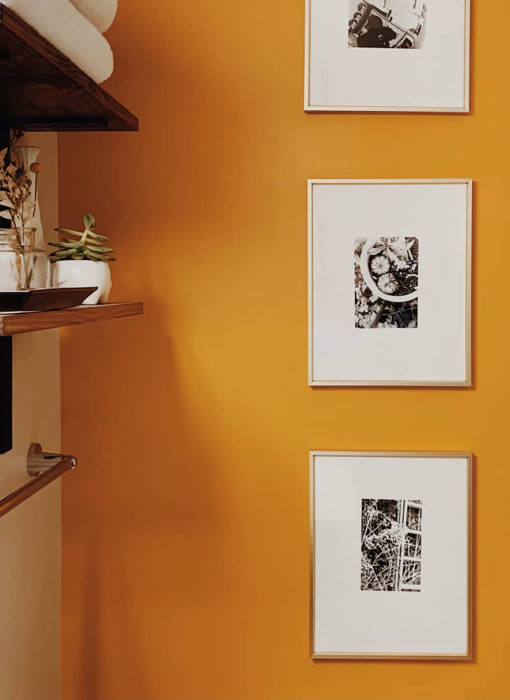 Bathroom wall with gold paint, shelves, and frames