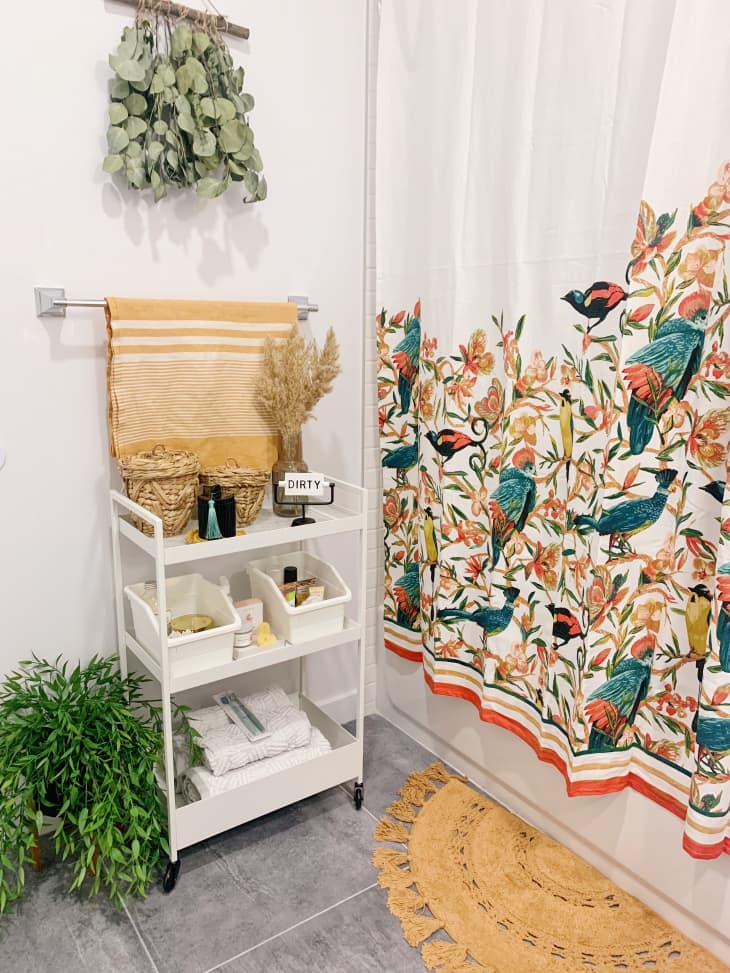 Bathroom with white cart, hanging eucalyptus, and shwoer curtain with bird print