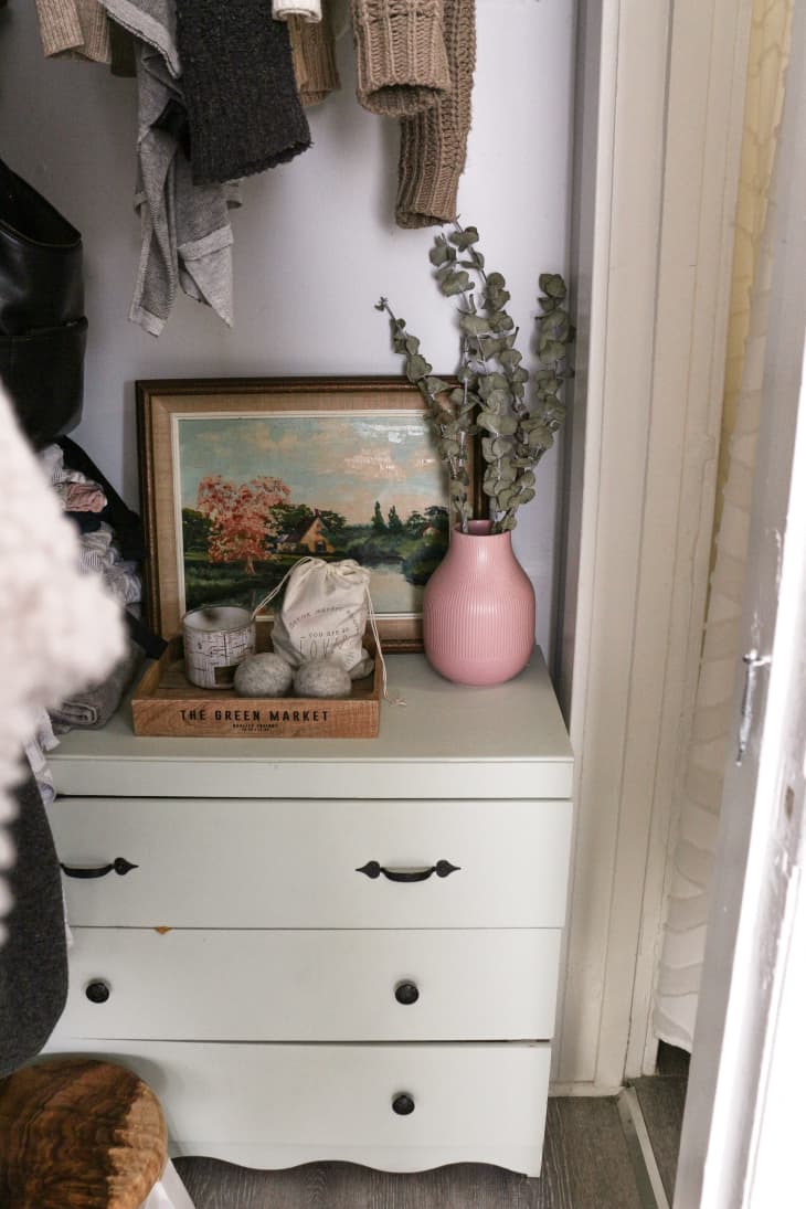 White dresser with vase of eucalyptus, decorative tray, and antique artwork on top