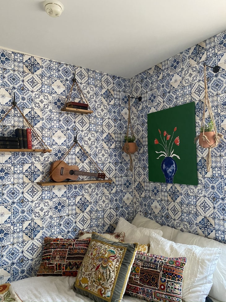 Bedroom with blue patterned wallpaper, shelves, and green artwork
