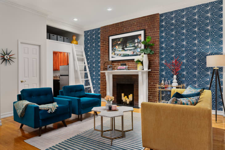 Living room with brick fireplace, blue wallpaper, yellow sofa, and teal armchairs
