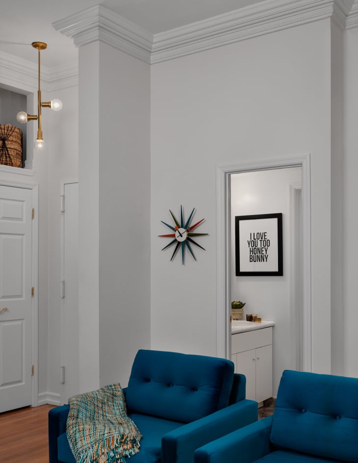 Entryway painted white with brass pendant light fixture and mid-century clock on the wall