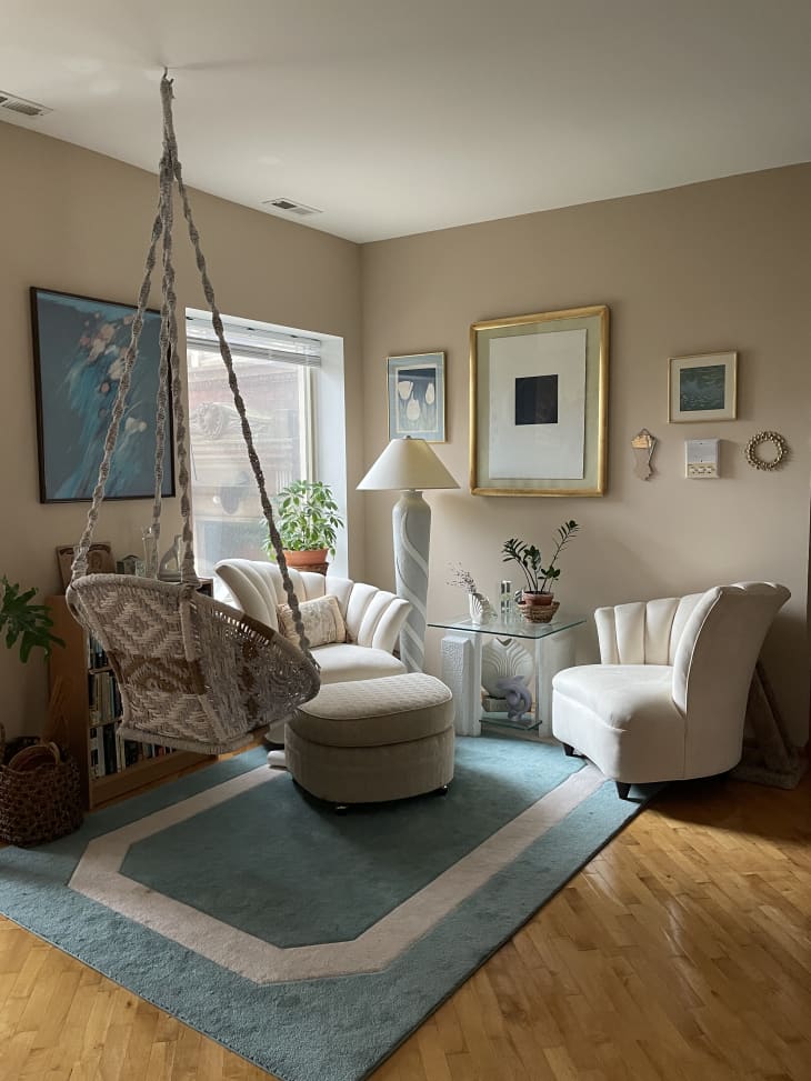 Reading corner with blue rug, rattan swing, and white shell-back chairs