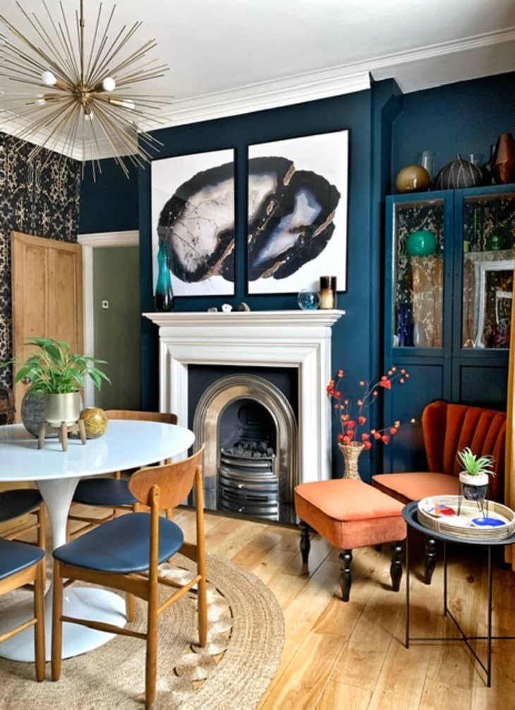Maximalist dining area with blue walls, starburst chandelier, and abstract artwork above fireplace