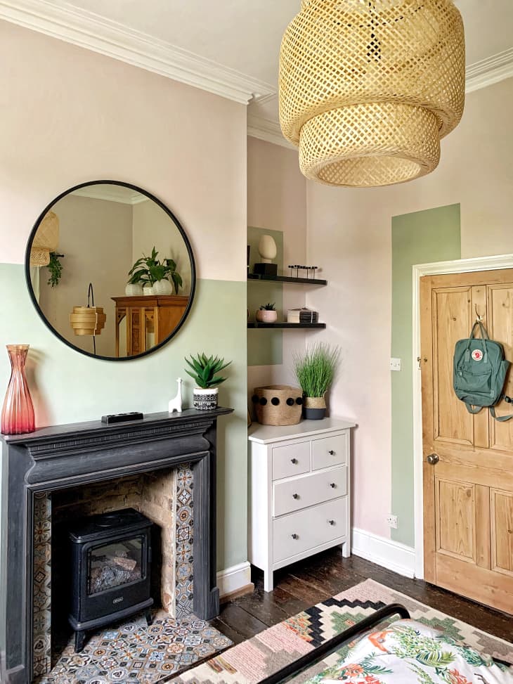 Bedroom entrance with light green colorblock paint, rattan pendant, and circular mirror above small black fireplace
