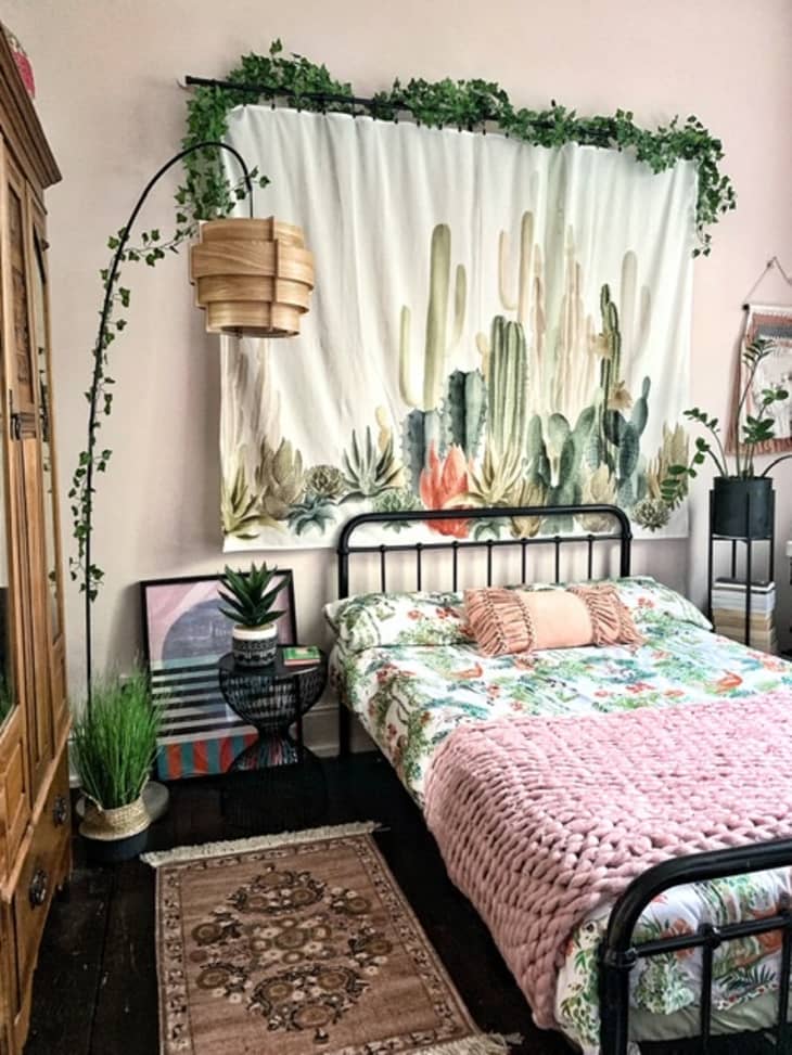 Bed with floral bedding beneath tapestry with cacti print