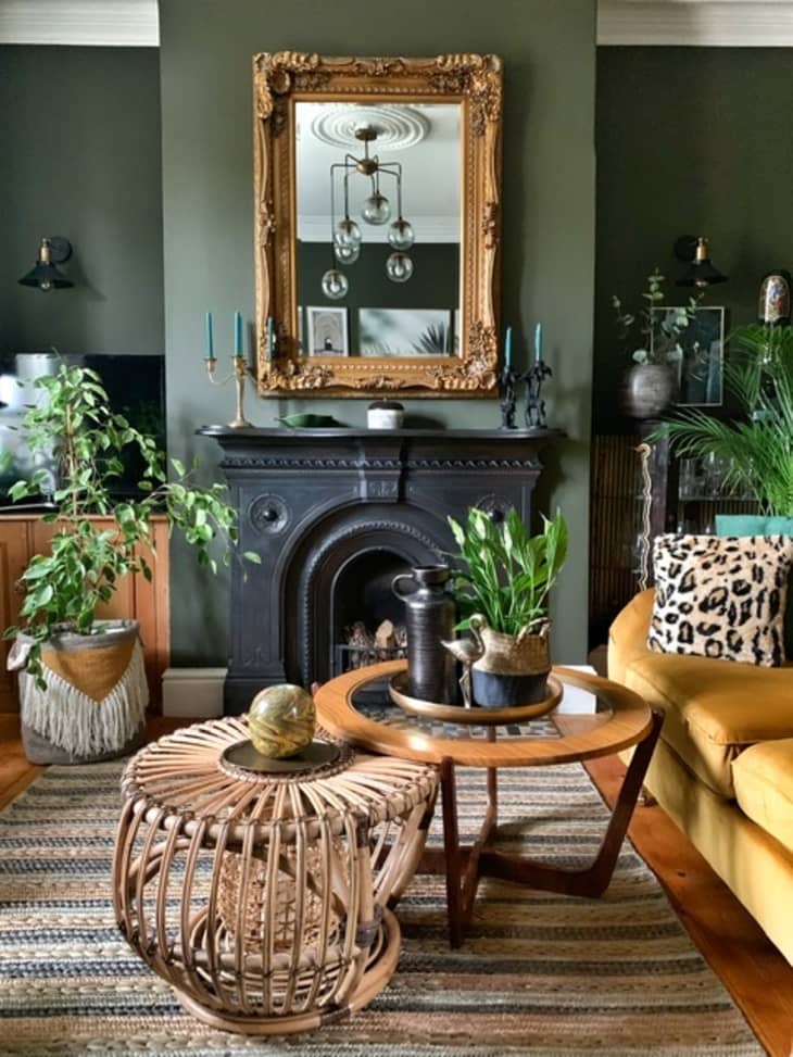 Living room with green walls, yellow sofa, large mirror above dark black fireplace, and two round coffee tables