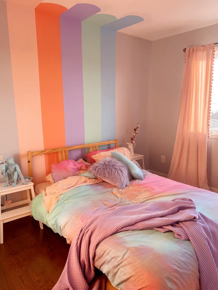 Pastel colored bedroom with pastel tie dye duvet and pastel rainbow mural behind an IKEA bed