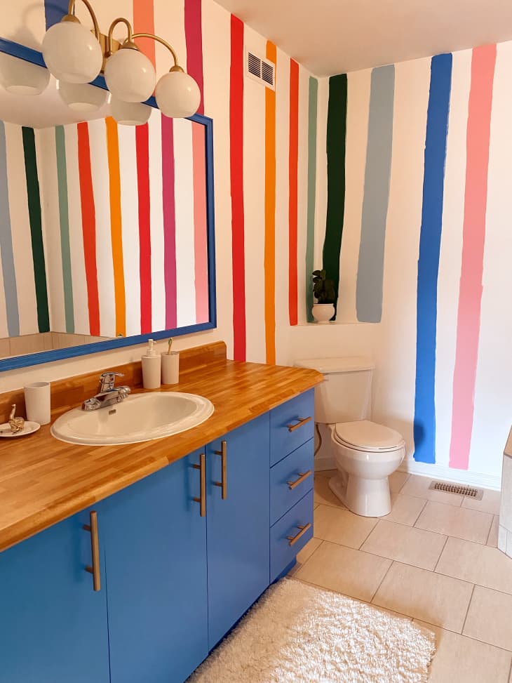 Bathroom with blue modern vanity and butcher block counter with hand painted wide colorful stripes on the walls