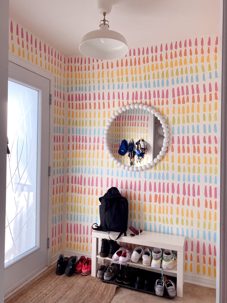 Entryway with white shoe shelf, white ball frame mirror, and rainbow stripe mural on the walls